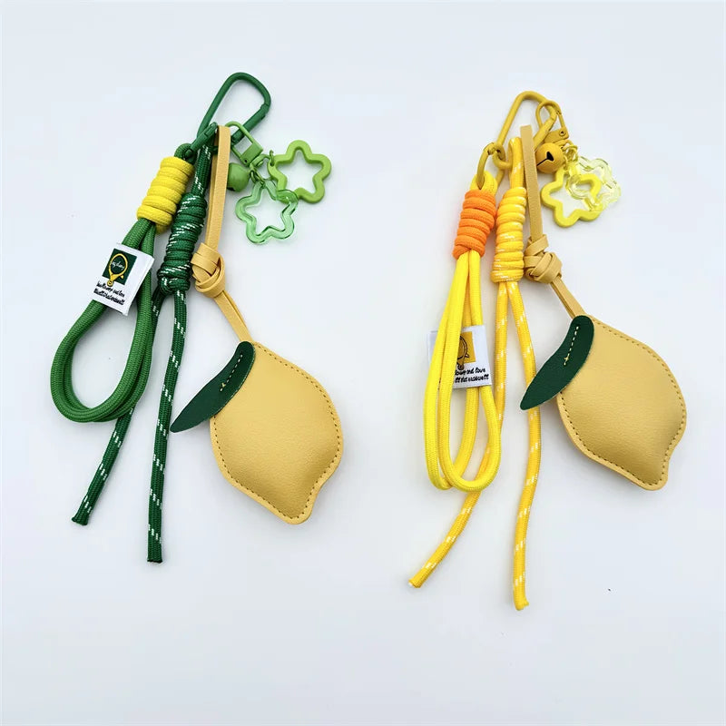 Two lemon-shaped keychains on a white background, one with green and yellow cords and one with yellow and orange cords, both featuring small flower charms and a small white brand tag.