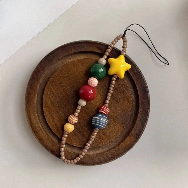 A wooden bead phone strap or necklace with a yellow star charm, displayed on a round wooden tray against a light off-white background.