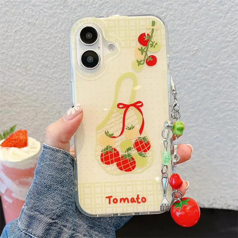 A hand holding a clear phone case decorated with a tomato-themed design, including a basket of red tomatoes and the word 'Tomato' in red text, with a dangling tomato charm.