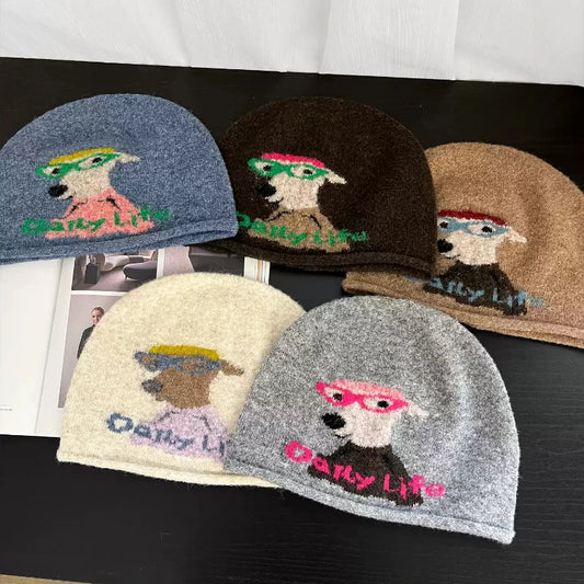 Five fuzzy knit beanies in different colors are arranged on a dark tabletop. Each beanie has a cartoon dog wearing sunglasses and the text 'Daily Life' knitted across the front.