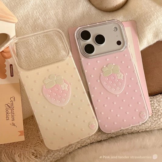 Two pastel phone cases with a strawberry motif, displayed on a soft beige fabric background. One case is cream/beige and the other is light pink, both featuring a 3D strawberry design and dotted texture.