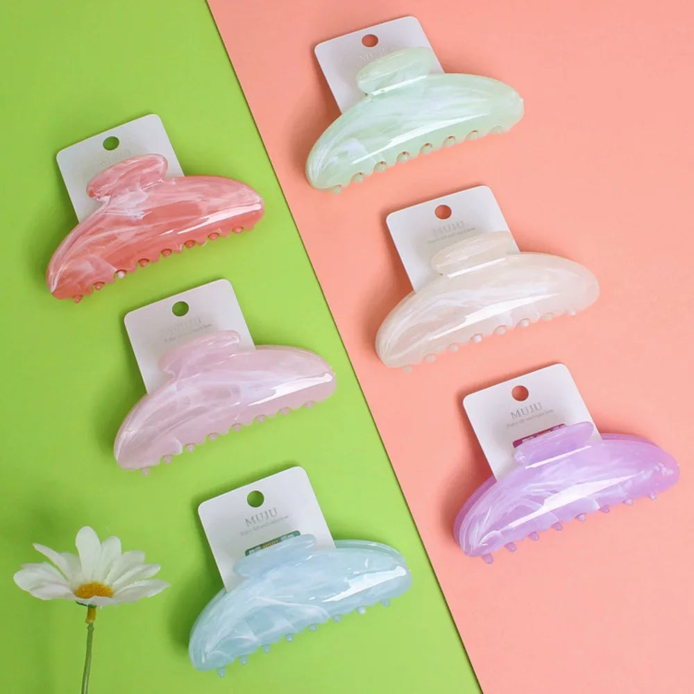 Set of colorful hair claw clips on a two-tone pink and green background with a daisy flower.