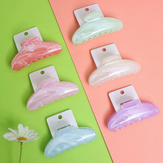 Set of colorful hair claw clips on a two-tone pink and green background with a daisy flower.