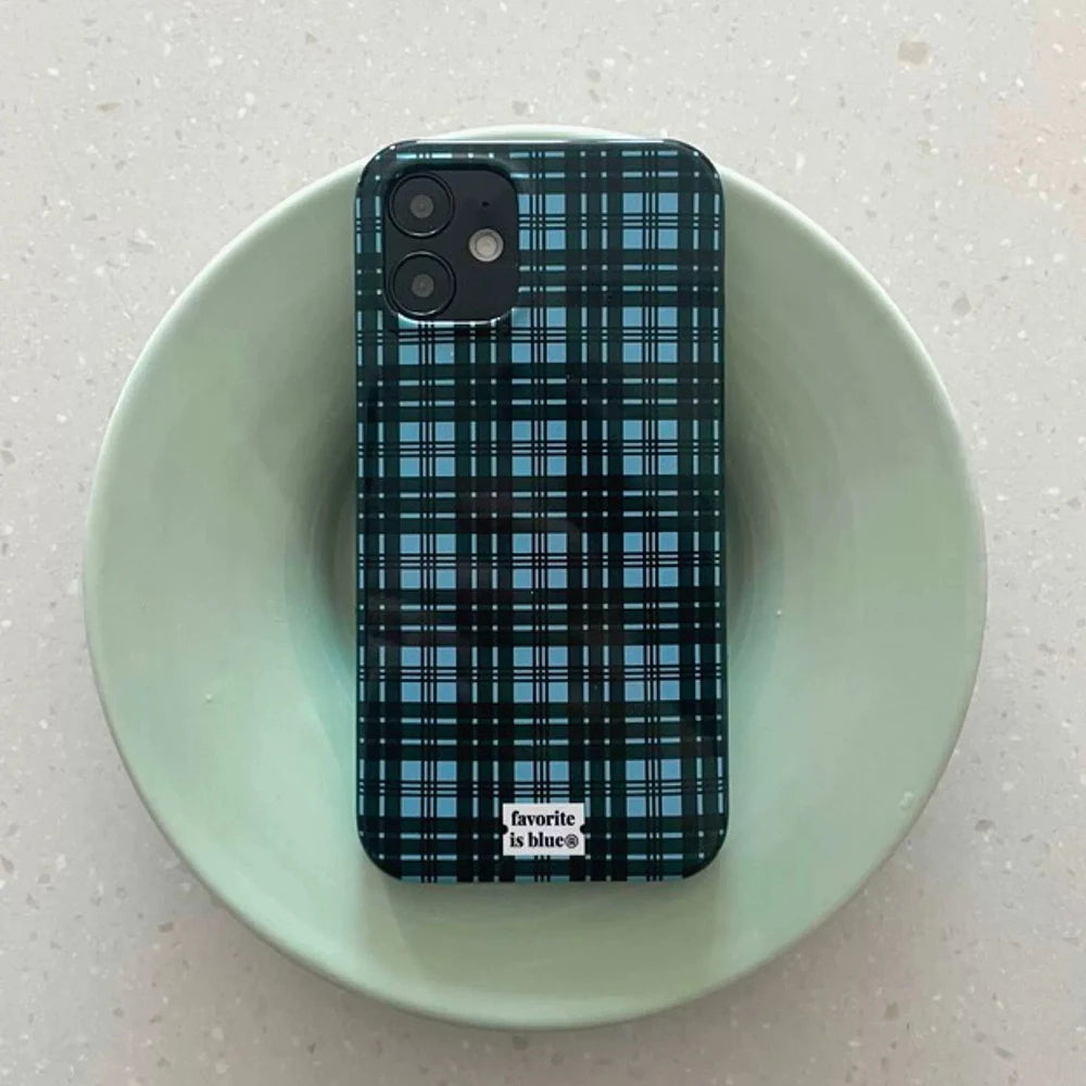 A smartphone case with a blue and black plaid pattern, shown on a phone resting inside a light green ceramic bowl on a speckled countertop. The brand name 'favorite is blue co.