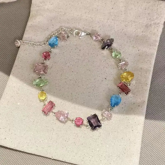 A multicolor gemstone bracelet with a silver chain and clasp, displayed on a textured beige fabric surface.