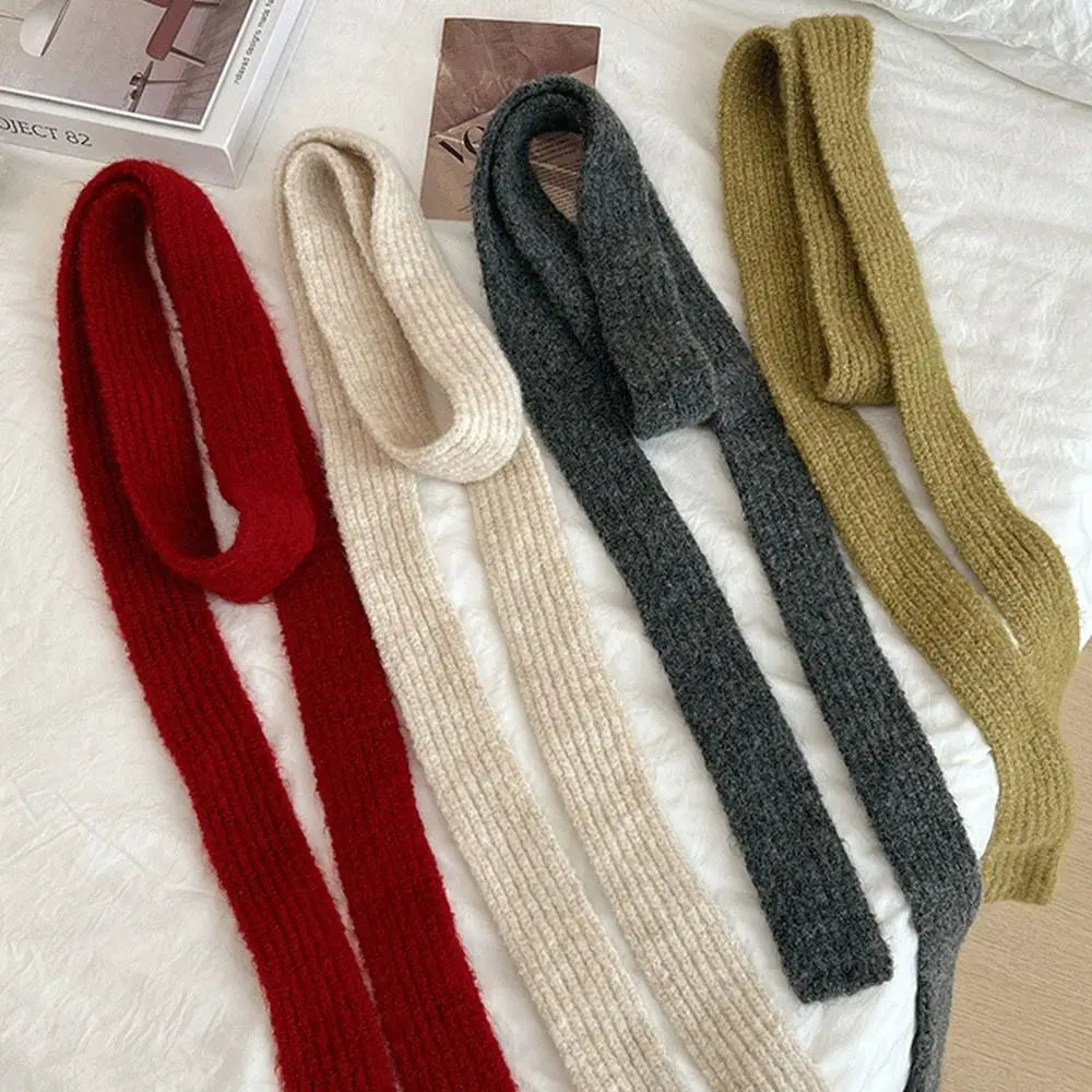 Four long, chunky knit shoulder straps or scarf-like accessories in red, cream, charcoal gray, and olive green, arranged diagonally on a white textured fabric surface.