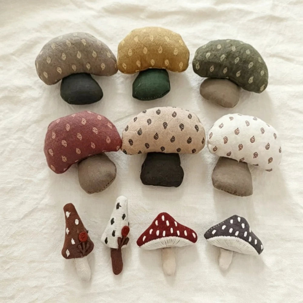 A set of nine handmade felt mushroom brooches in various colors and patterns, arranged on a textured off-white fabric background.