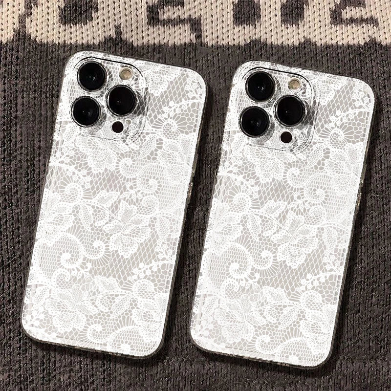 Two white phone cases with an intricate floral lace pattern, shown on the back of silver smartphones, resting on a dark textured knit surface.