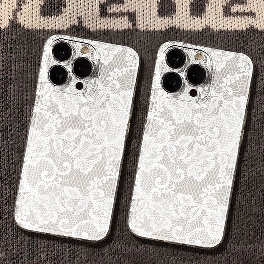 Two white phone cases with an intricate floral lace pattern, shown on the back of silver smartphones, resting on a dark textured knit surface.