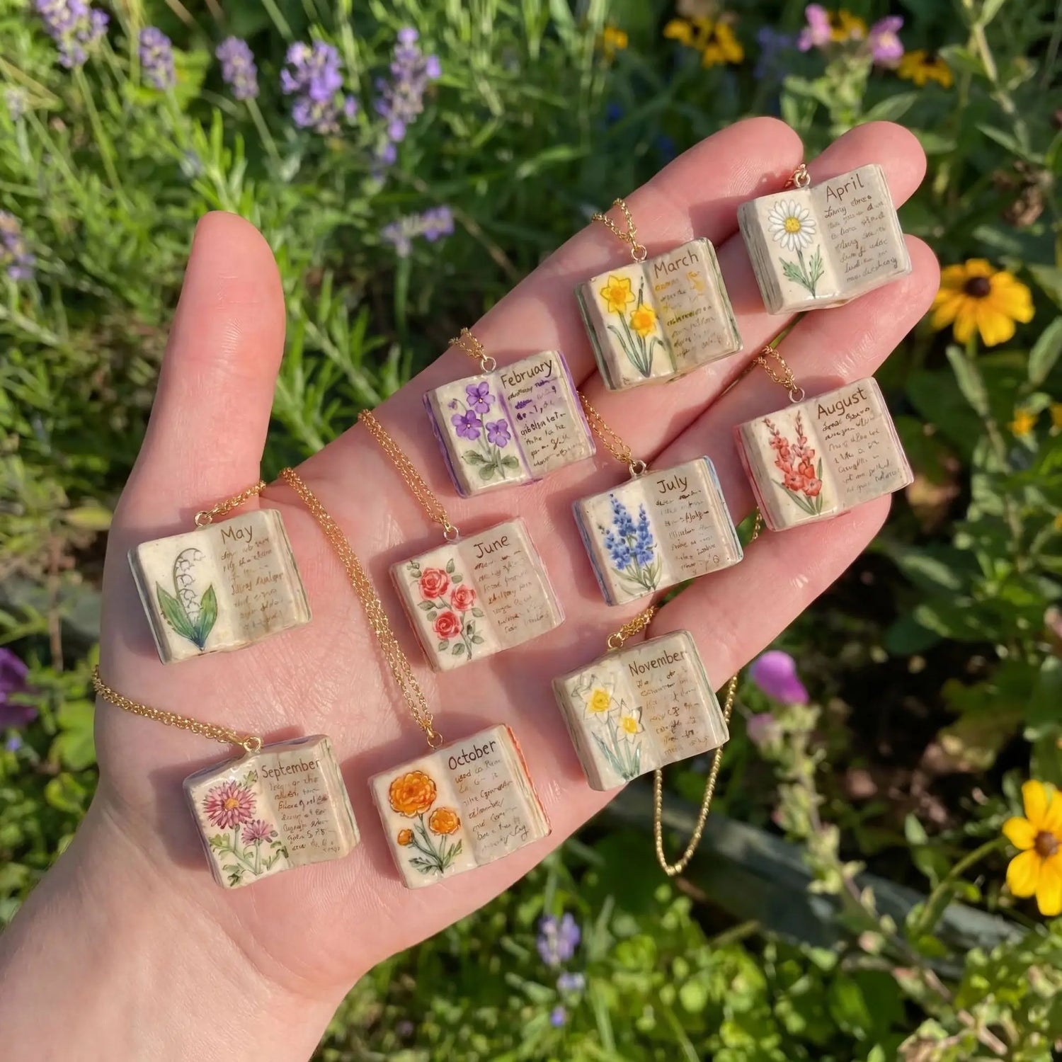 Hand holding a collection of small books with floral designs and months printed on them, set against a natural background.