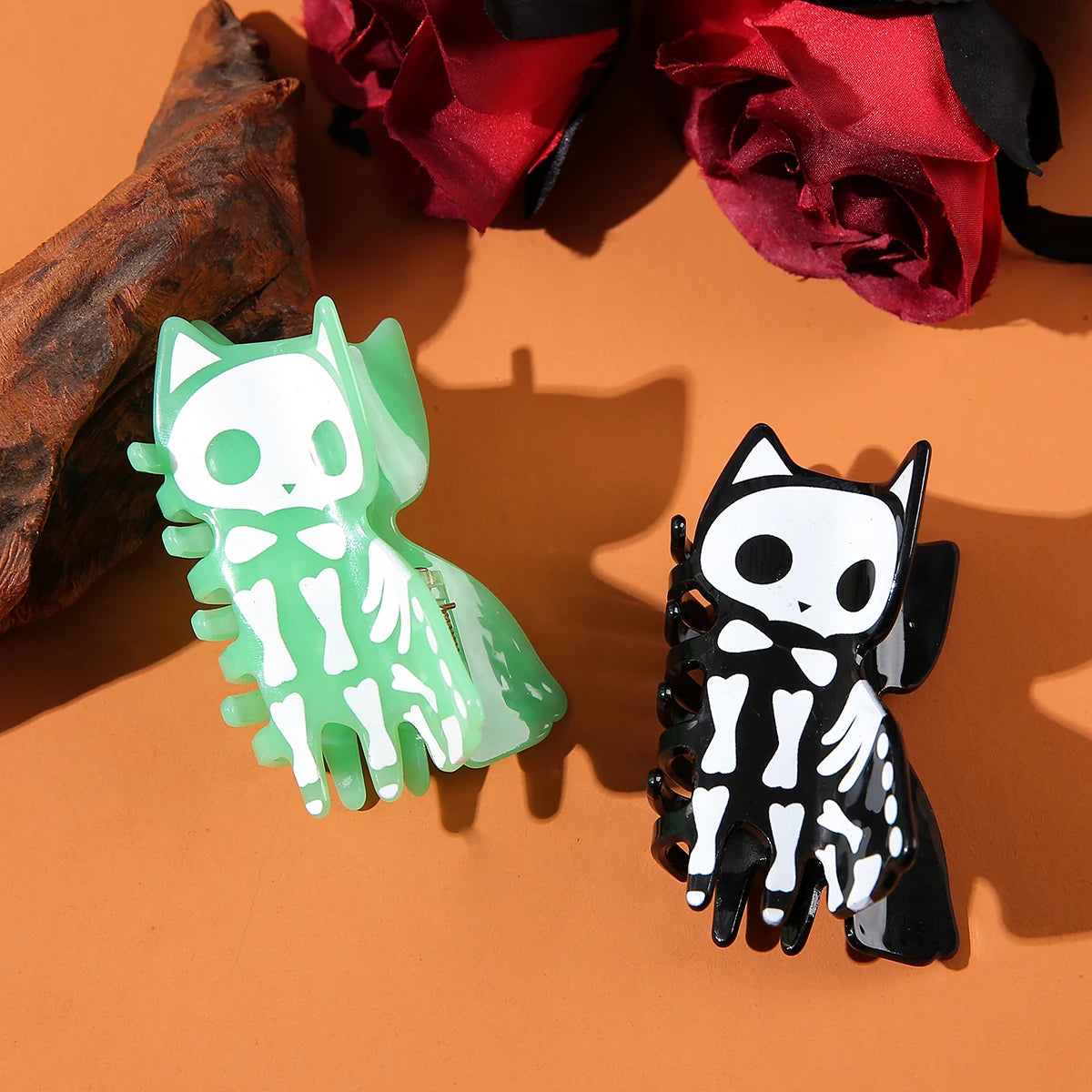 Two skeleton-themed hair clips on an orange surface with red flowers in the background.