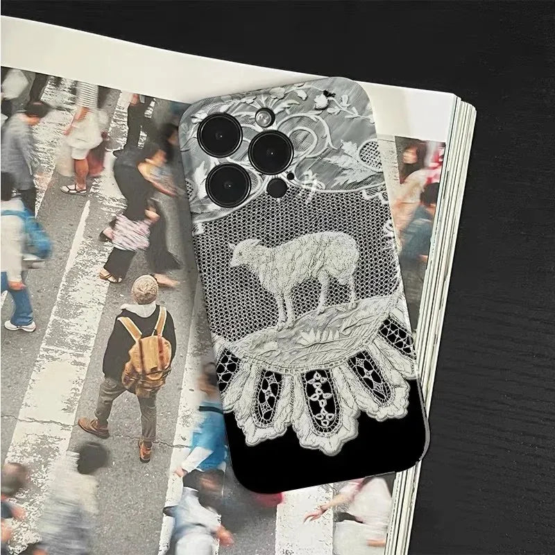 A smartphone case with a black and white lace and sheep design, shown resting on top of an open magazine with blurred street-crossing photos.
