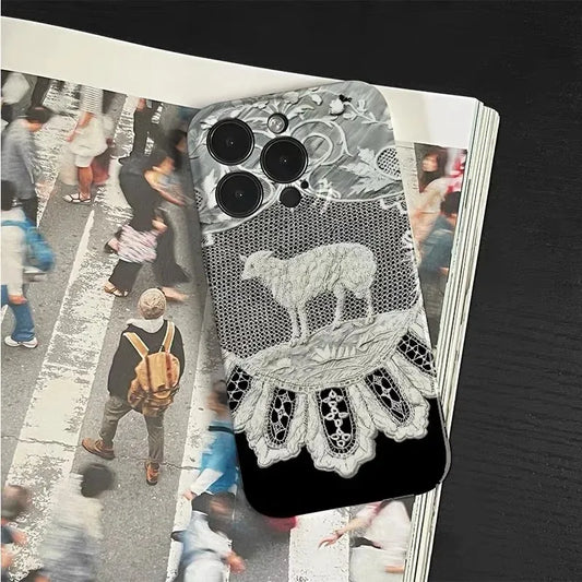 A smartphone case with a black and white lace and sheep design, shown resting on top of an open magazine with blurred street-crossing photos.