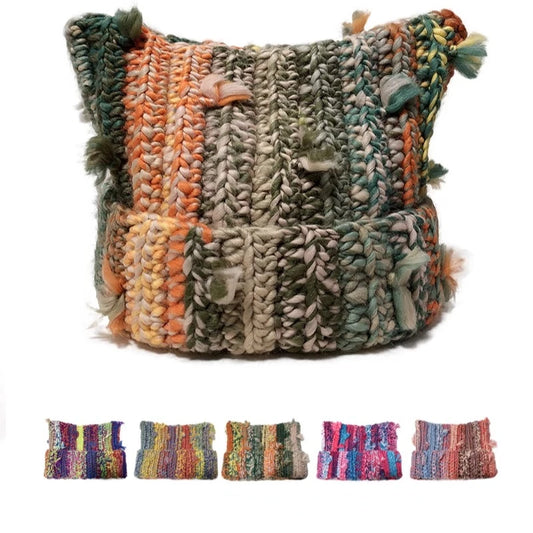 A chunky handwoven cat ear beanie in a multicolor variegated yarn with stripes of green, orange, beige, and gray, featuring tassels on the sides. Five smaller color variant thumbnails are shown along the bottom on a white background.