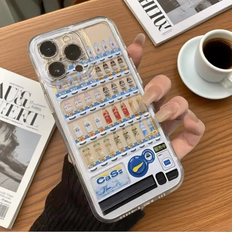 Phone case with vending machine design held by a hand on a table with a newspaper and coffee cup.
