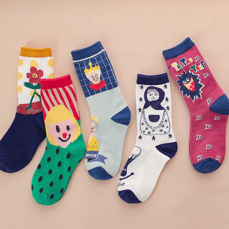 Five pairs of children's patterned socks arranged in a row on a solid pale pink background. The socks feature various cartoon and character designs including a flower, a clown, a princess, a queen, and a lion.