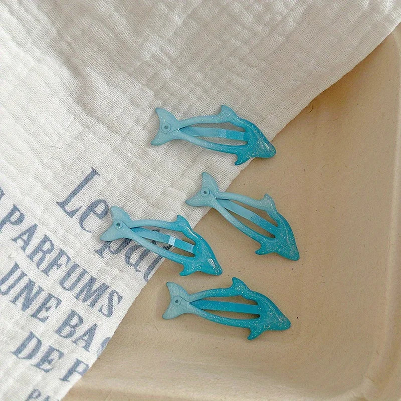 Blue dolphin-shaped hairclips on a beige surface with a white fabric background.