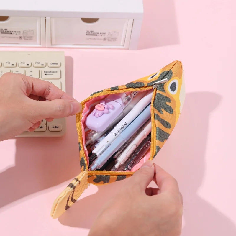 Person holding a small, colorful fish-shaped pouch with stationery items on a pink surface.