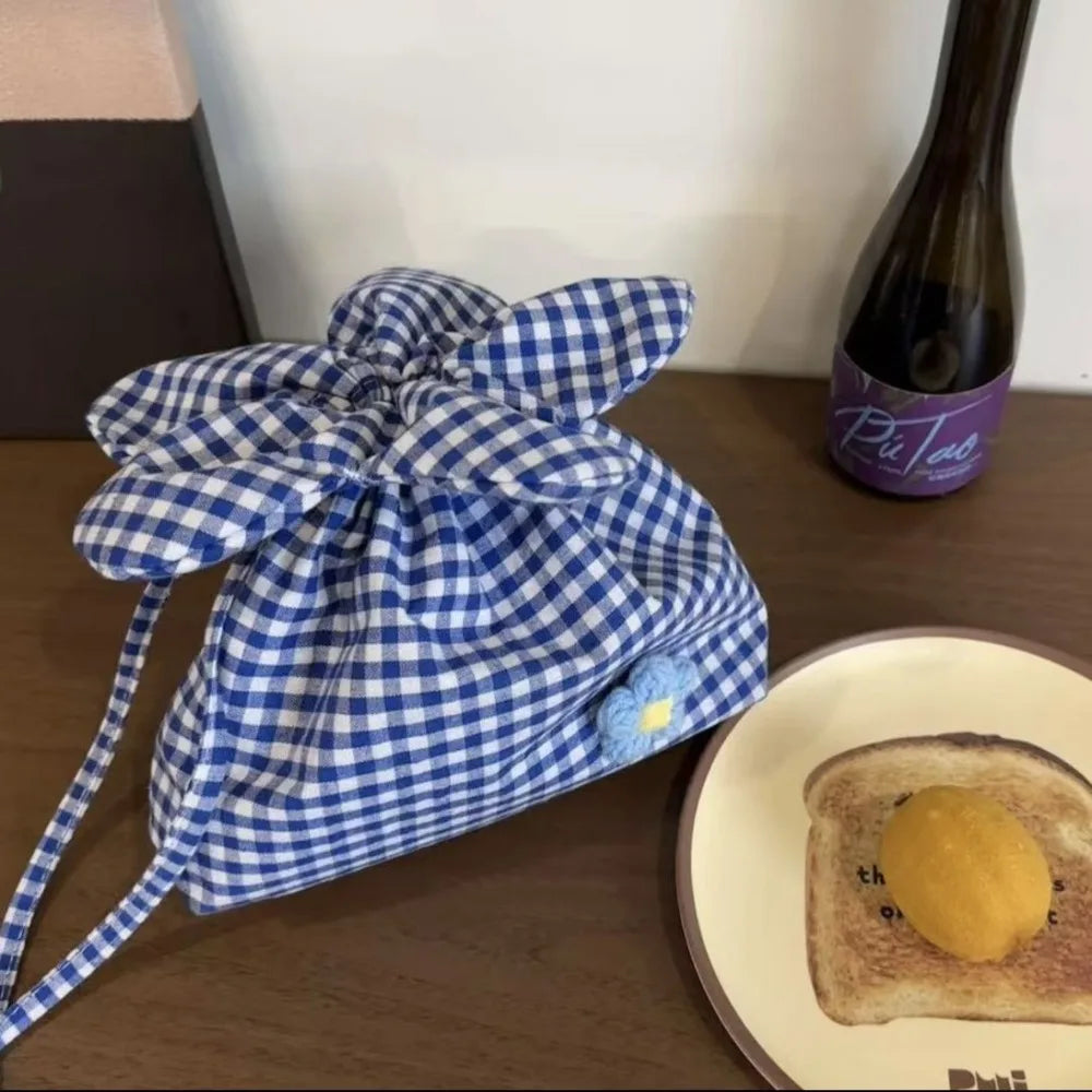 Blue and white checkered drawstring bag on a table with toast and a bottle in the background