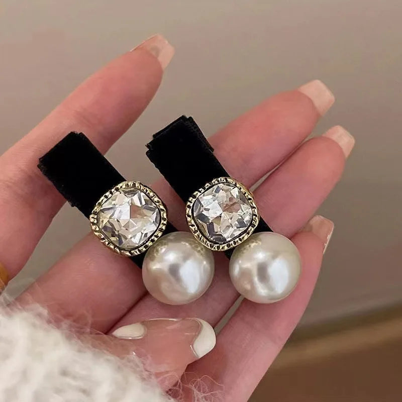Hand holding two decorative hair clips with crystal and pearl design.