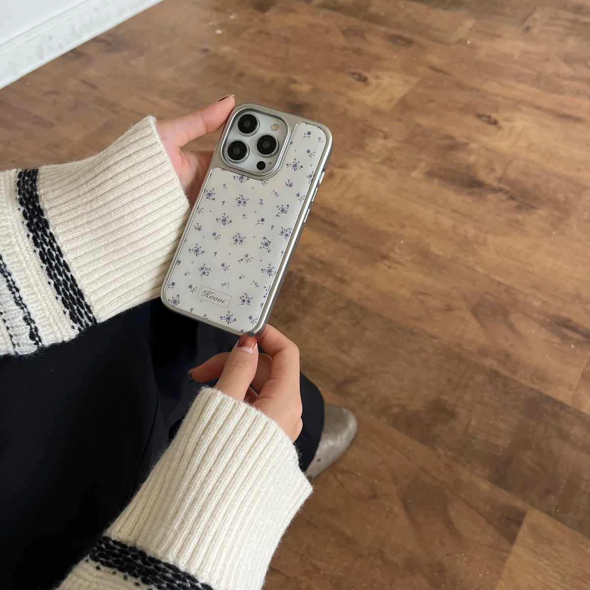 Person holding a phone with a floral case on a wooden floor