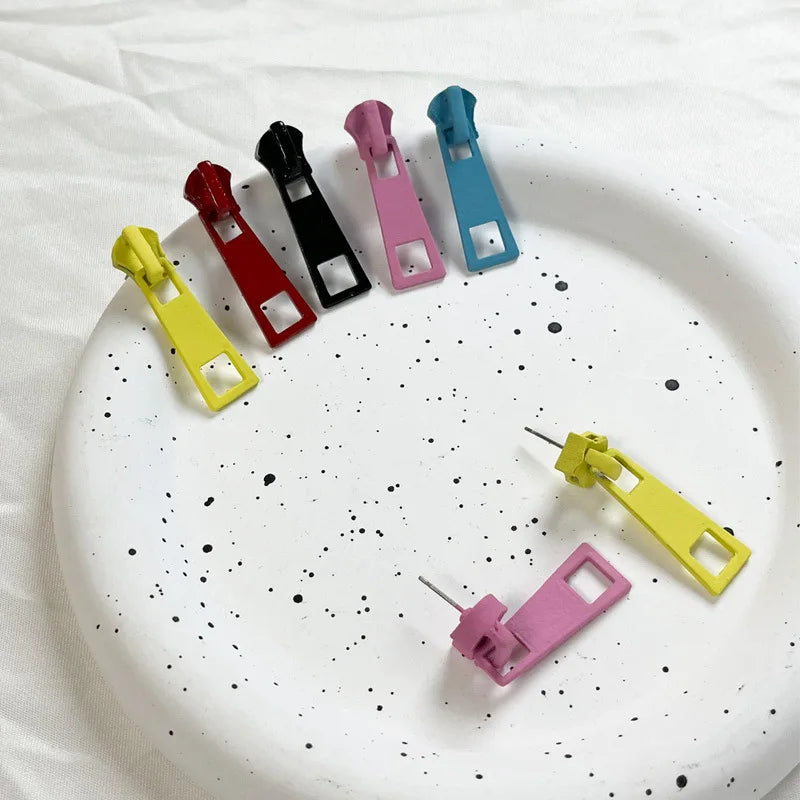 Six small plastic clip-like accessories in yellow, red, black, pink, and blue are arranged on a white speckled plate over a white fabric background.