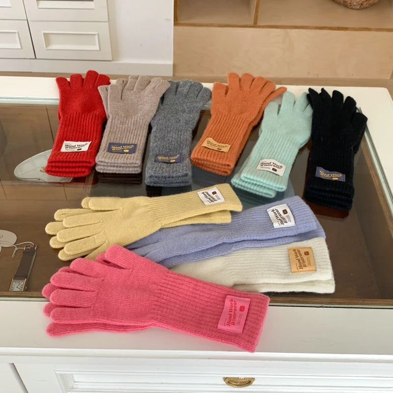 A set of nine multi-colored knit gloves arranged on a glass-topped table. The gloves come in red, light gray, charcoal gray, orange, mint green, black, pale yellow, lavender, cream, and bright pink.