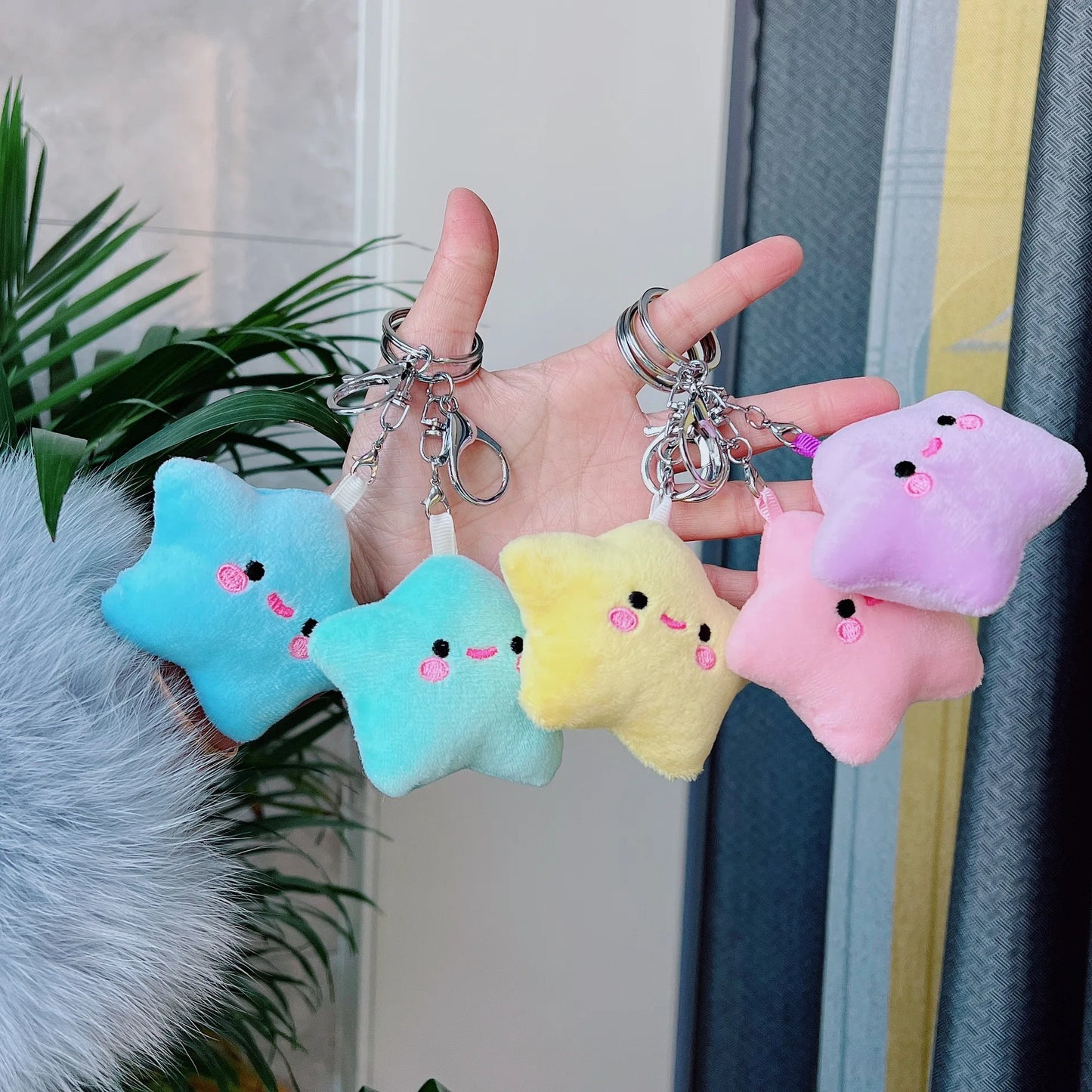 Hand holding five colorful star-shaped keychains with a neutral background