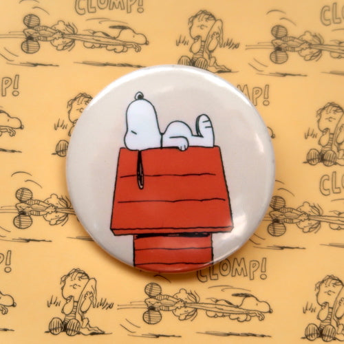 A vintage style pin button badge featuring Snoopy the beagle from the Peanuts comics asleep on his dog house