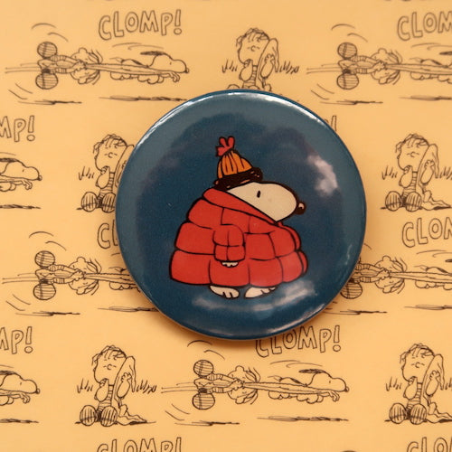 A vintage style pin button badge featuring Snoopy the beagle from the Peanuts comics wearing a puffy coat