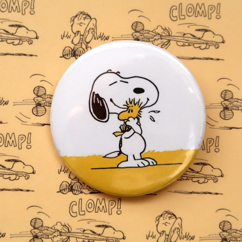 A vintage style pin button badge featuring Snoopy the beagle from the Peanuts comics hugging Woodstock