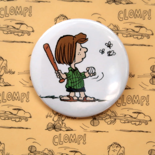 A vintage style pin button badge featuring a picture of Peppermint Patty the beagle from the Peanuts comics playing baseball