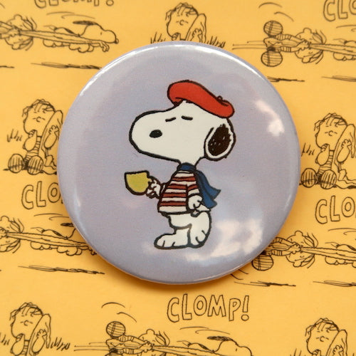 A vintage style pin button badge featuring Snoopy the beagle from the Peanuts comics wearing a French inspired outfit