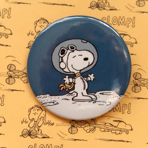 A vintage style pin button badge featuring Snoopy the beagle from the Peanuts comics in an astronaut costume on the moon
