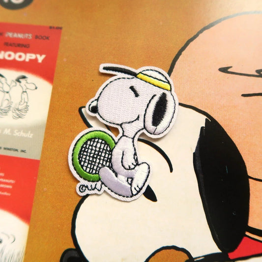 Patch of a dog holding a tennis racket with a character in the background