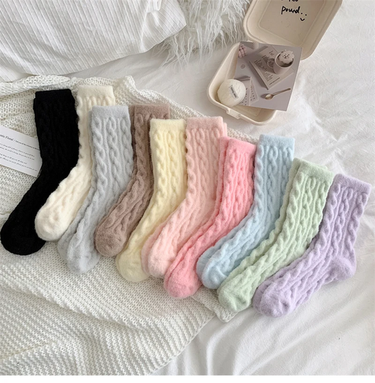A collection of fluffy cable knit crew socks in various pastel colors displayed on a bed with a tag and a small container beside them.