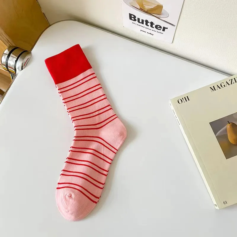 Pink sock with red stripes on a white surface next to a magazine