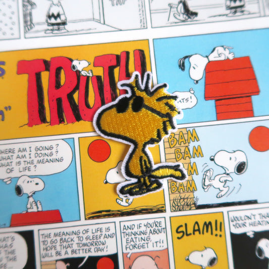 An embroidered patch depicting the character Woodstock from Snoopy/Peanuts comics, wearing sunglasses, on a yellow background resembling a comic strip.