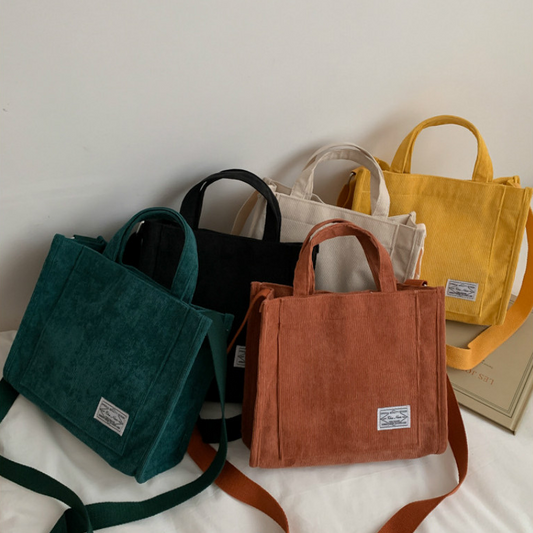 A collection of five Corduroy mini tote bags in beige, black, green, brown, and yellow, displayed with handles and shoulder straps visible.