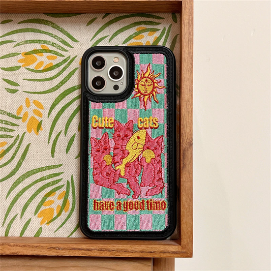 A black embroidered iPone case featuring an embroidered illustration of pink cats with fish and balls and a yellow sun under "cute cats have a good time" lettering slogan
