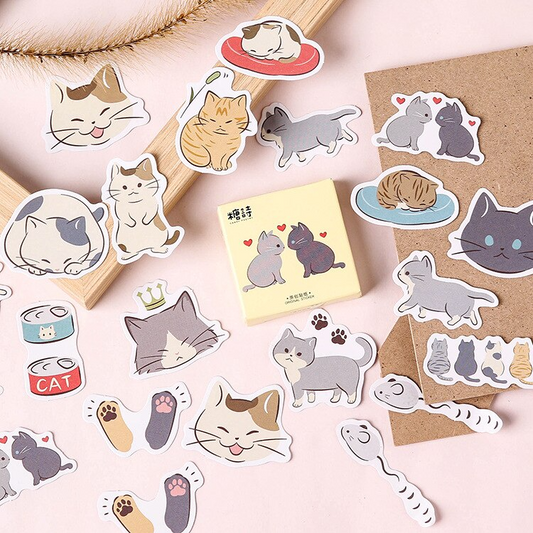 A collection of various illustrated cat stickers placed on a surface near a cardboard box with a sticker on it.