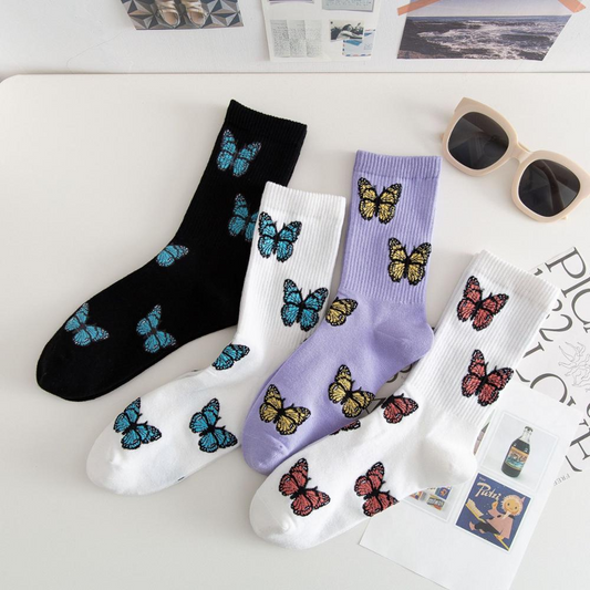 A collection of crew socks in black, white, and various colors featuring butterfly patterns, displayed on a table with sunglasses and paper items in the background.