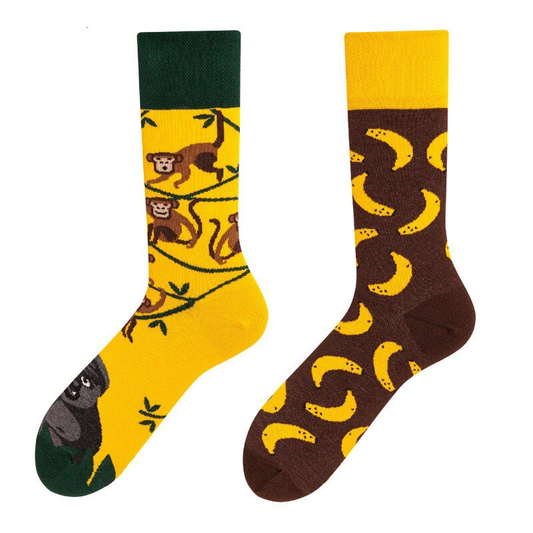 A pair of mismatched crew socks with one featuring a monkey design in green and the other with a banana pattern in yellow and brown.